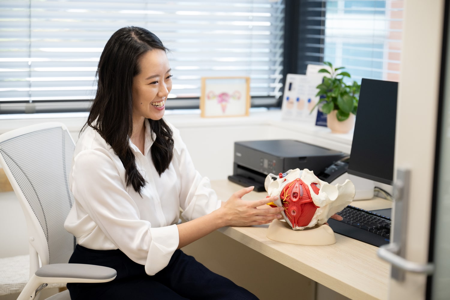 a woman sitting at a desk pointing at a model of a human body